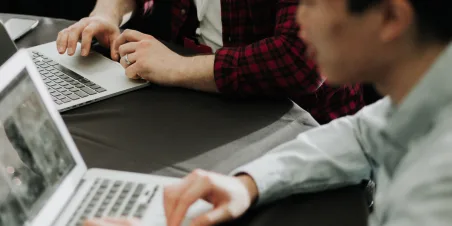 Photo: Two men working on their laptops together.