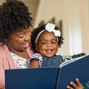 Photo: Mother reading to a smiling toddler who is sitting on her lap.