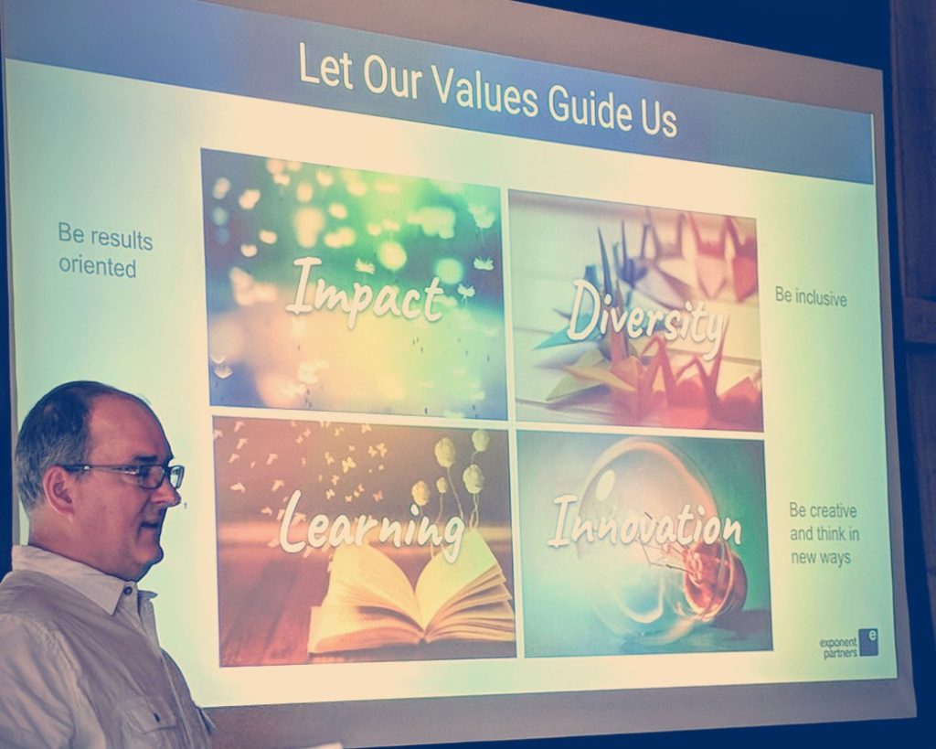 Photo: Founder Rem Hoffmann stands in front of a projection screen that lists our values: diversity, learning, innovation, and impact.