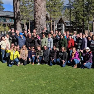 Photo: Staff standing together on grassy lawn and waving at the camera.