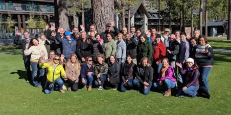 Photo: Staff standing together on grassy lawn and waving at the camera.