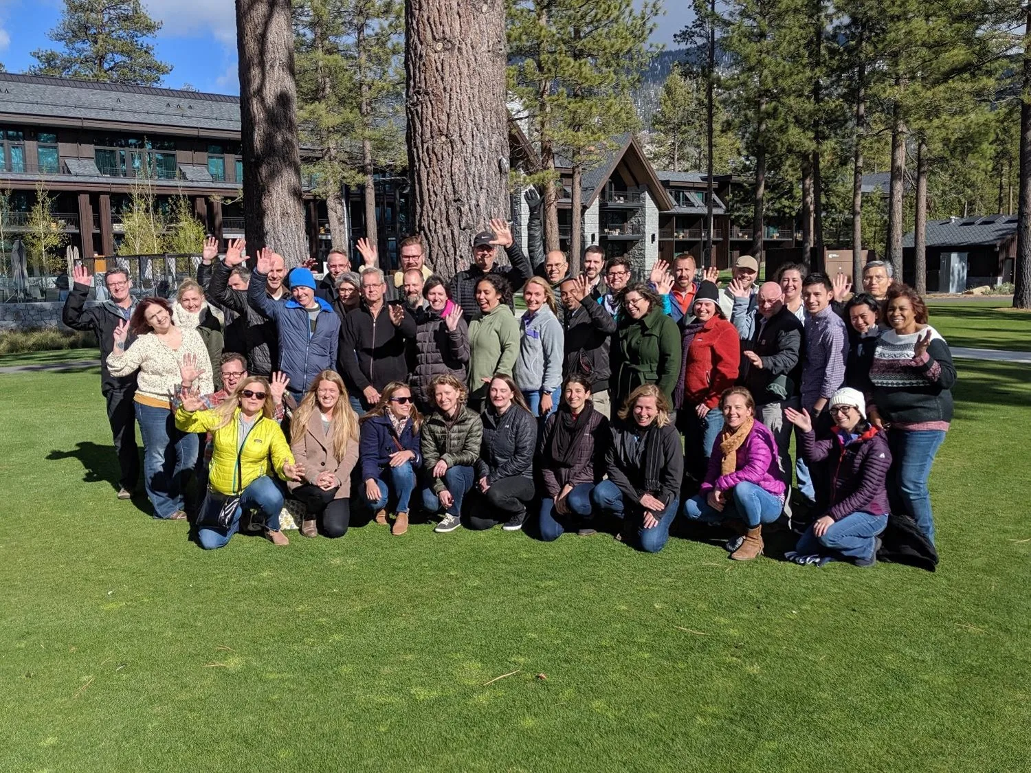 Photo: Staff standing together on grassy lawn and waving at the camera.