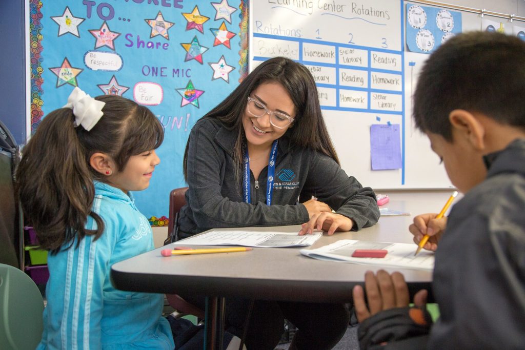 Photo: Instructor helping two children with skills worksheets.
