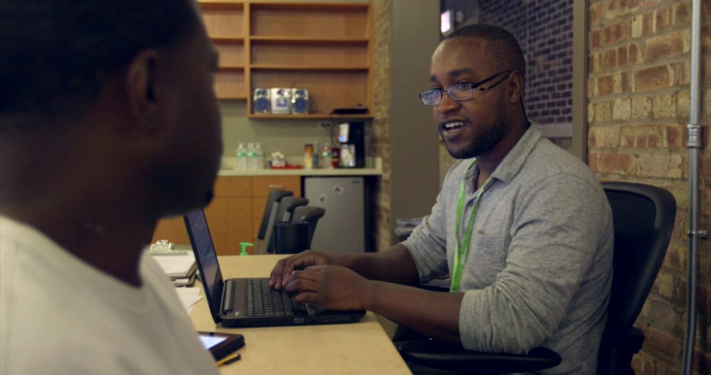 Photo: Breakthrough staff member sitting with partner and entering data into laptop.