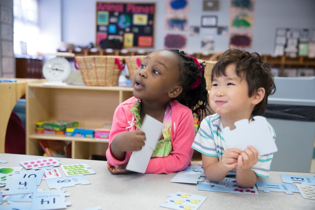 Photo: Two school children sit at table playing with cards.