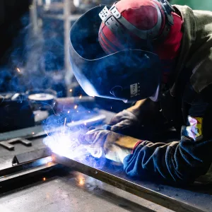 Photo: Member of workforce welding metal in factory workshop.