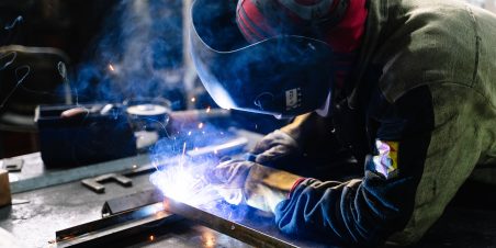 Photo: Member of workforce welding metal in factory workshop.