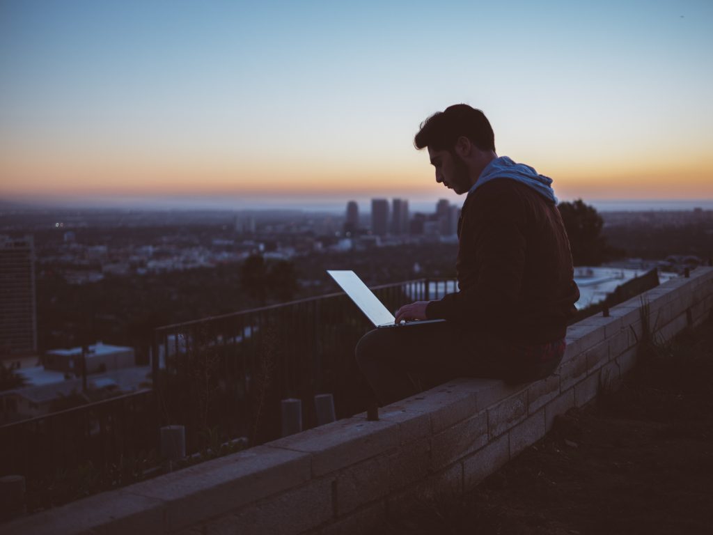 Photo: man sitting on rooftop remotely working from laptop