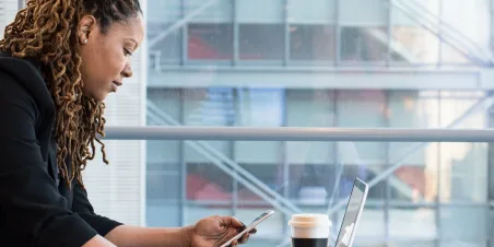 Photo: Woman with smartphone and coffee conducting remote work.