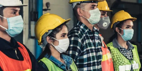 Photo: Men and women warehouse workers standing next to each other while wearing protective masks.