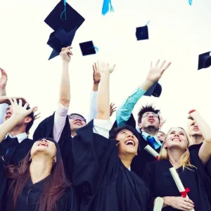 Photo: happy graduates tossing caps in the air and smilign while holding new diplomas