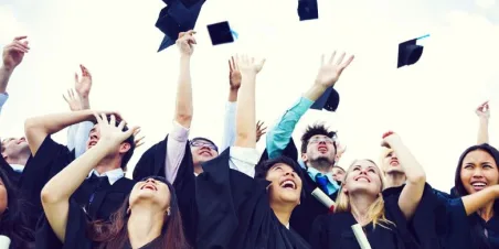 Photo: happy graduates tossing caps in the air and smilign while holding new diplomas