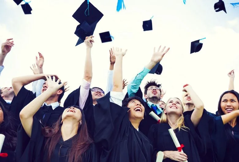 Photo: happy graduates tossing caps in the air and smilign while holding new diplomas