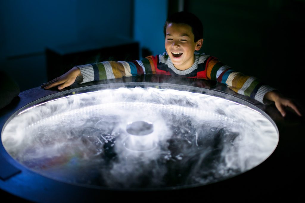 Photo: Young boy smiling enjoying a science exhibit at The Exploratorium.