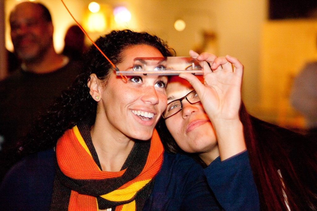 Photo: Two women smiling looking through the prism glass at the Exploratorium.